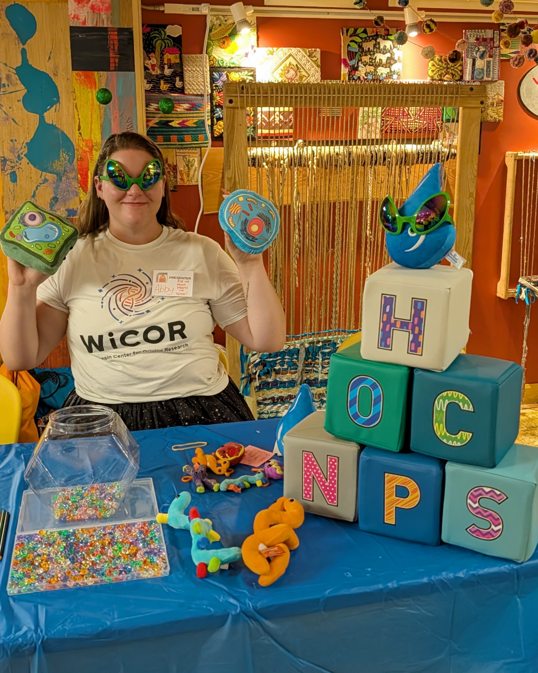 A postdoc poses with element blocks for CHONPS and stuffed DNA, RNA, cell parts, and cells.