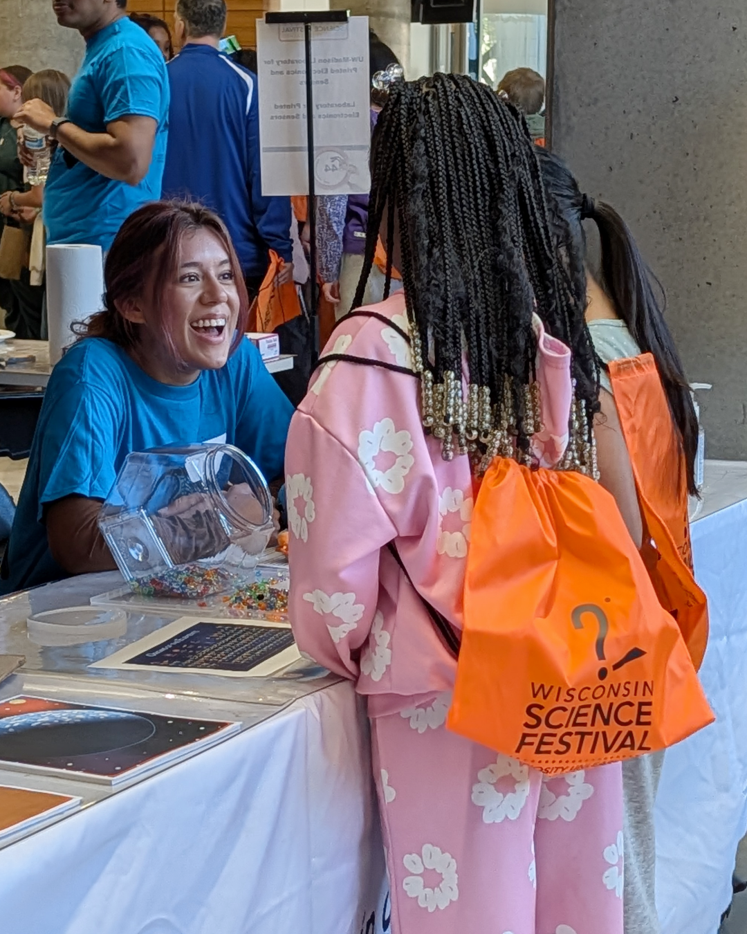 A smiling undergraduate student talks to two children about a WiCOR science station activity
