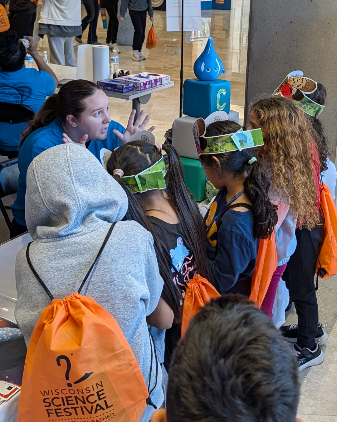 A WiCOR Graduate Student talks to a group of children, many wearing bug headbands, about WiCOR science