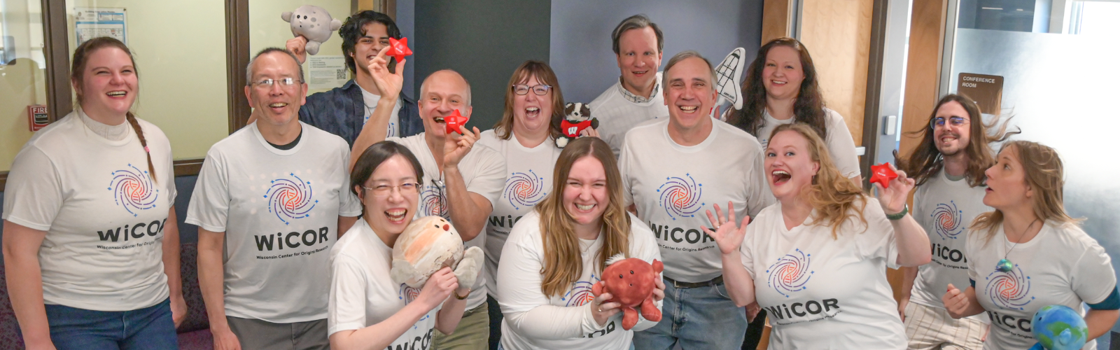 Group photo of WiCOR students, faculty and staff in the WiCOR space, having fun and holding stuffed animals of stars, planets, a space shuttle and Bucky Badger.